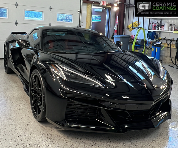 A front three-quarter view of a dark grey luxury sedan parked in a bright detailing garage, showcasing dark tinted windows and a highly reflective, polished finish.