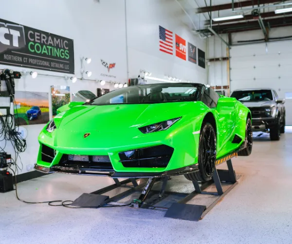 green Lamborghini supercar elevated on a hydraulic lift inside a professional garage featuring a "CT Ceramic Coatings" sign, as seen in paint protection film