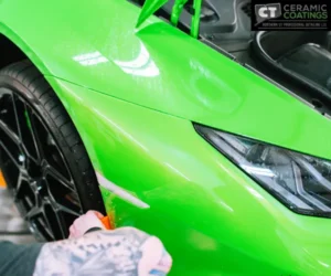 green Lamborghini supercar elevated on a hydraulic lift inside a professional garage featuring a "CT Ceramic Coatings" sign, as seen in paint protection film