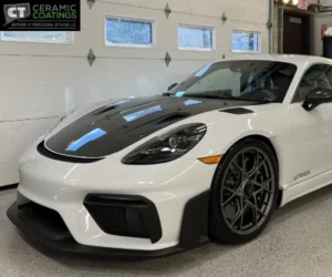 view of a white Porsche sports car with a carbon fiber hood parked in a clean detailing bay, as shown in paint correction