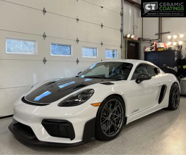 view of a white Porsche sports car with a carbon fiber hood parked in a clean detailing bay, as shown in paint correction