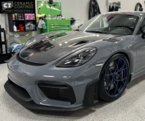 view of a gloss grey Porsche sports car with a dark hood parked next to detailing supplies and green tool carts, as seen in paint protection film