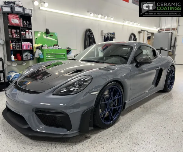 view of a gloss grey Porsche sports car with a dark hood parked next to detailing supplies and green tool carts, as seen in paint protection film