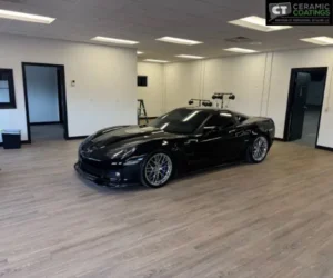 Wide side view of a black Corvette displayed inside a clean, climate-controlled indoor vehicle storage unit with neutral walls