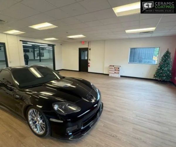 Wide side view of a black Corvette displayed inside a clean, climate-controlled indoor vehicle storage unit with neutral walls