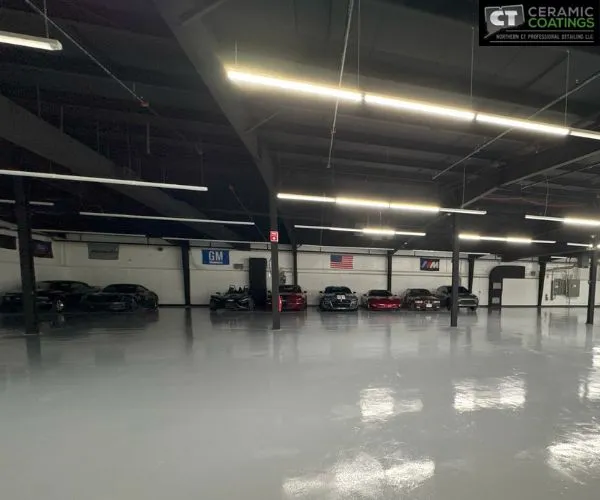 Wide interior shot of a spacious climate-controlled storage facility with polished grey floors housing multiple luxury and sports cars