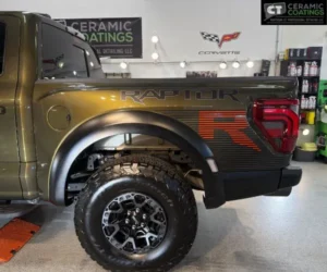 Close-up side view of the rear bed and wheel of an olive-green Ford Raptor featuring red and black body graphics.