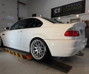 Rear side view of a glossy white BMW M3 coupe parked inside an auto detailing garage.